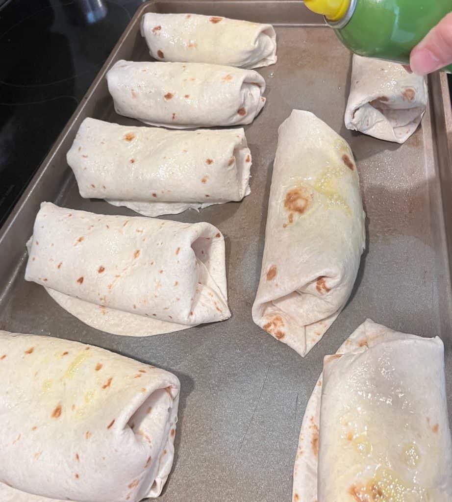 chimichangas on pan being sprayed with oil